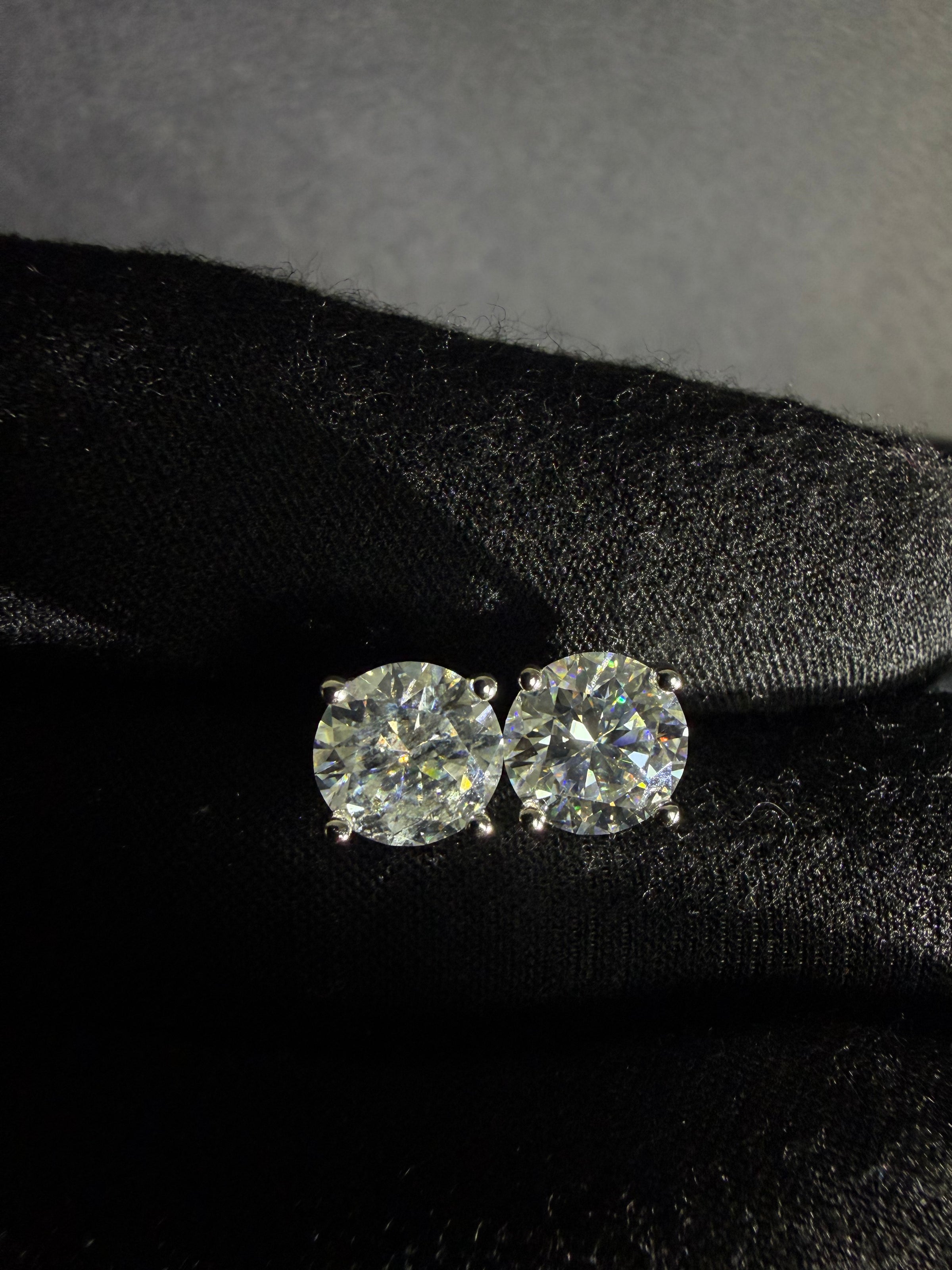 Round moissanite stud earrings in sterling silver photographed on black fabric