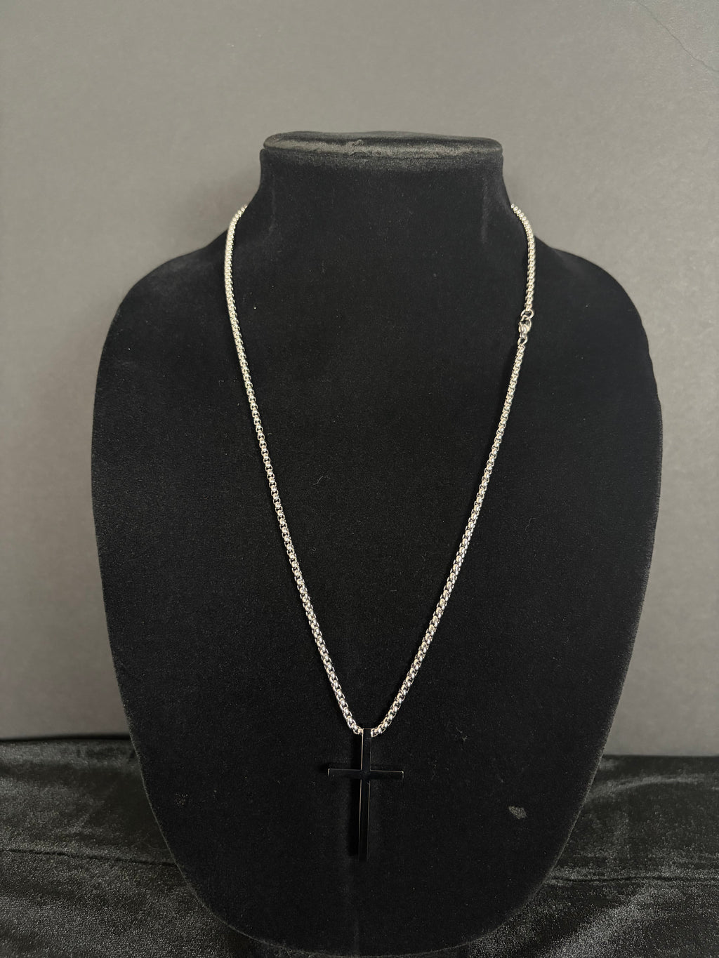 Silver-tone cross necklace — front view on a black display