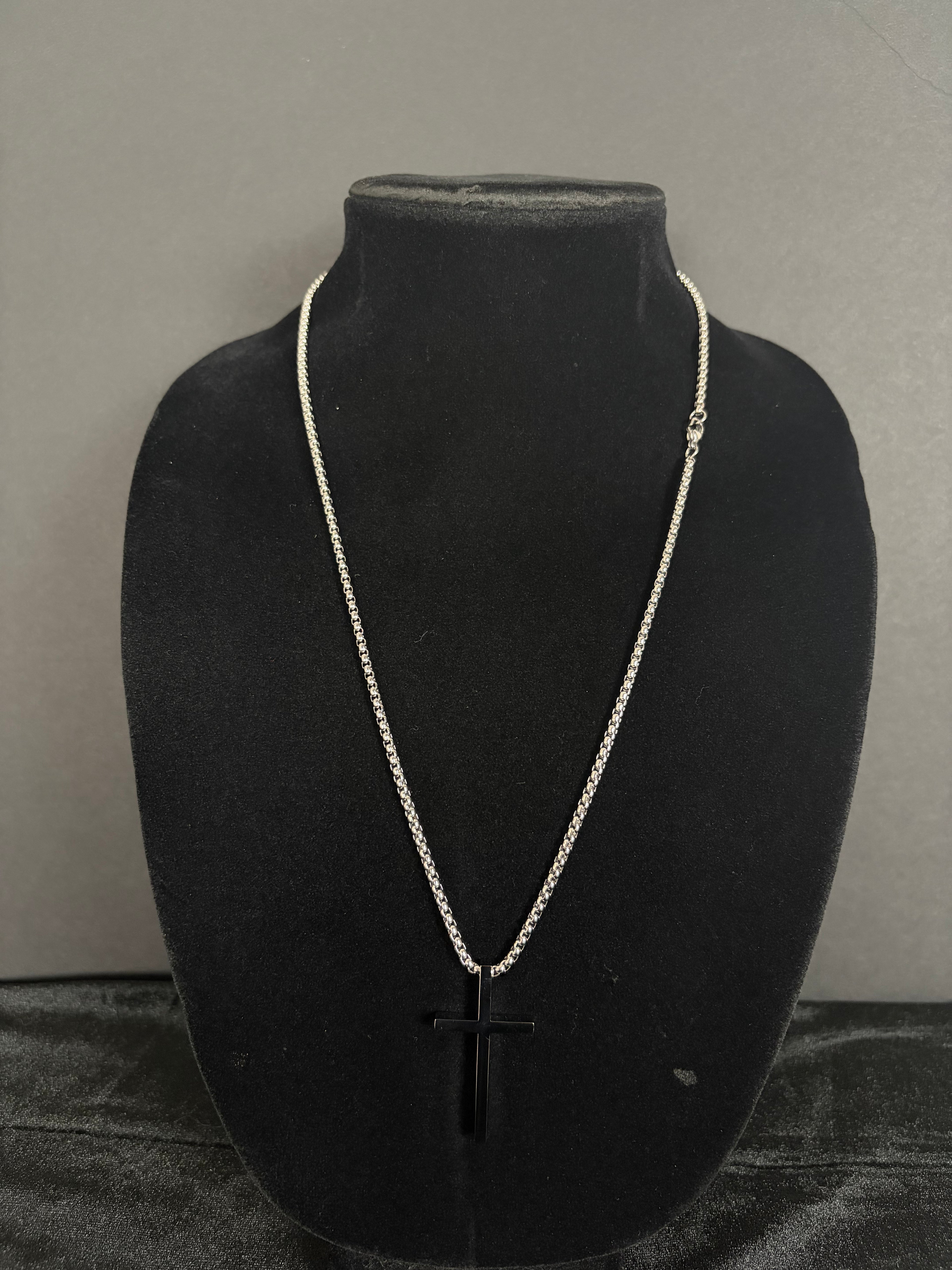 Silver-tone cross necklace — front view on a black display