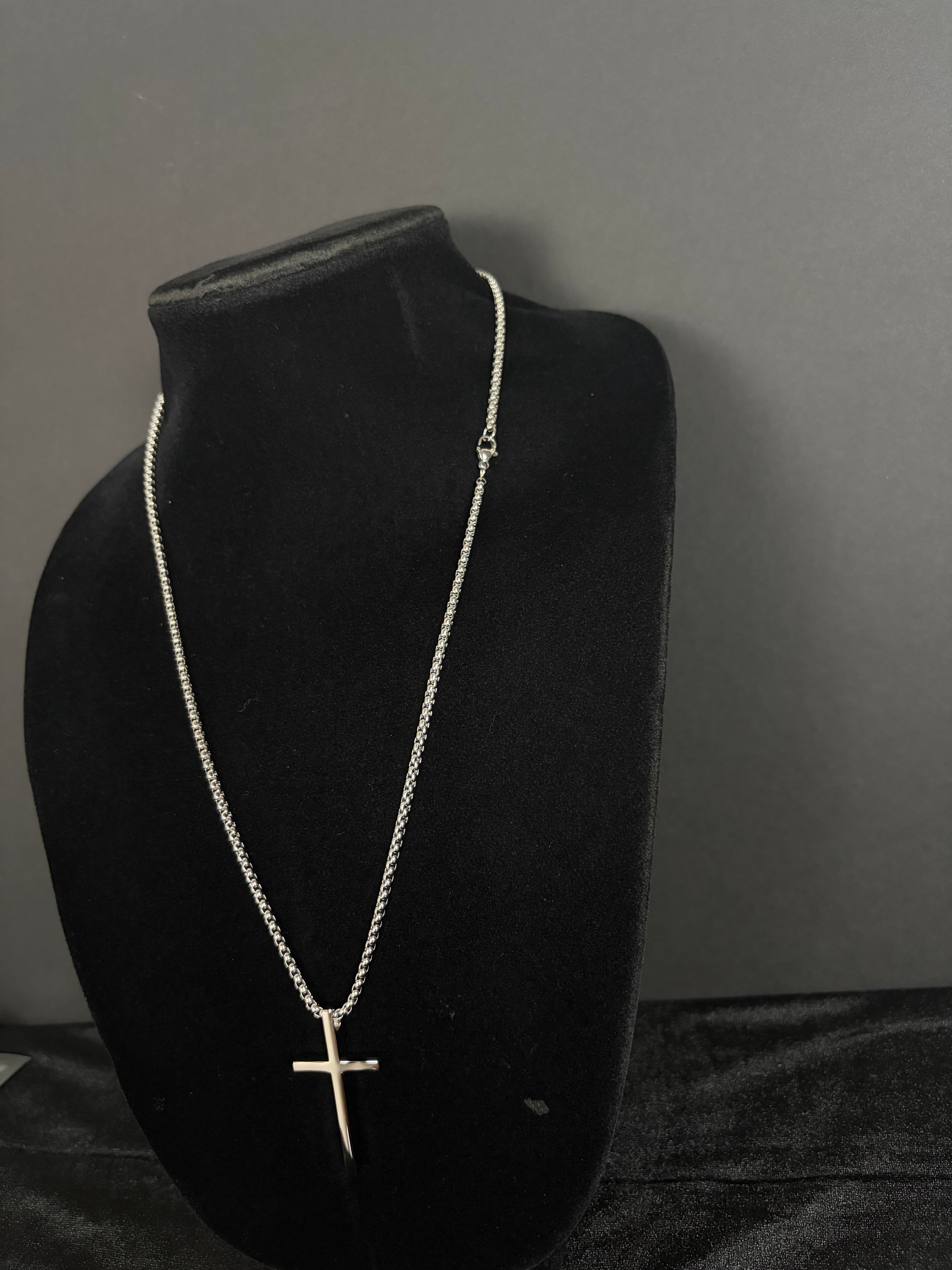 Silver-tone cross necklace — angled view on a black display